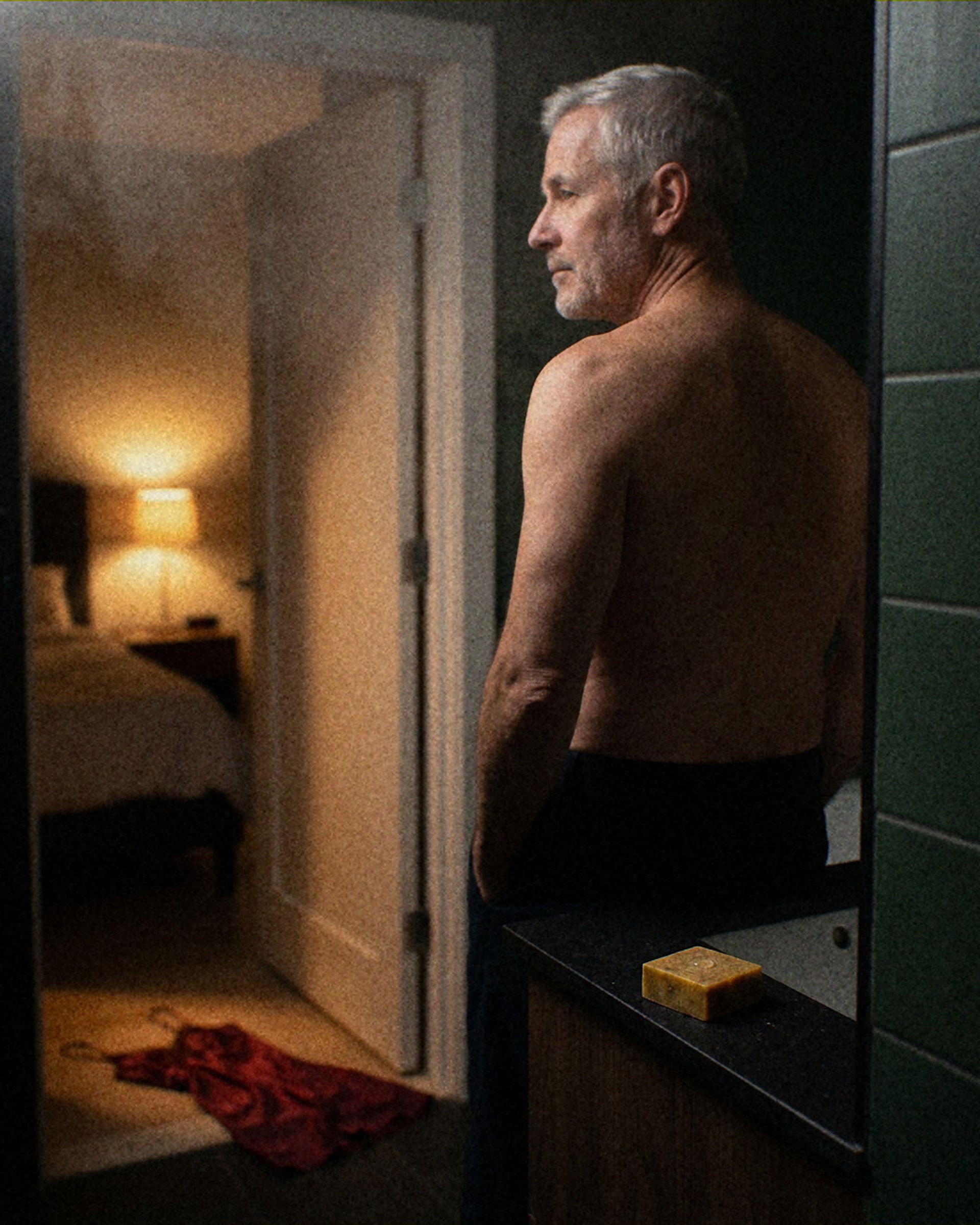 A grey-haired man at his bathroom door at night, a bar of Jungle Bravo soap on the counter and a red slip on the floor