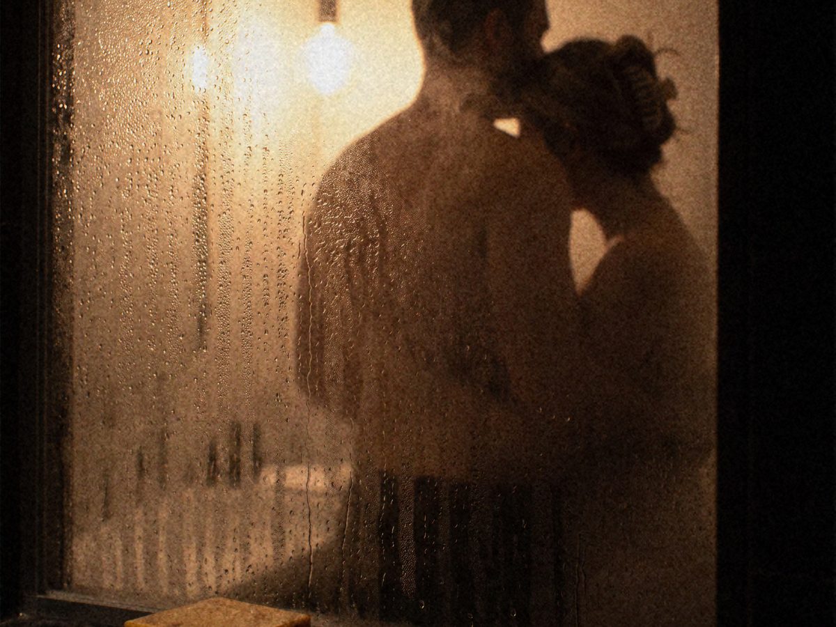 A couple embracing behind a steamed shower door, a bar of Jungle Bravo soap on the ledge